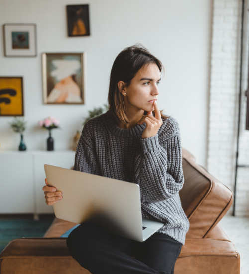 person holding laptop with finger on mouth thinking